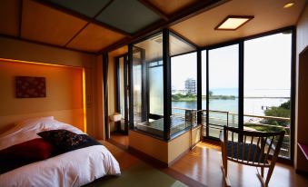a bedroom with a bed , tatami mat floor , and a view of the ocean through large windows at Biwako Ryokusuitei
