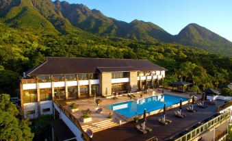 a large resort with a pool and lounge chairs is nestled in the mountains , surrounded by trees at Sankara Hotel & Spa Yakushima