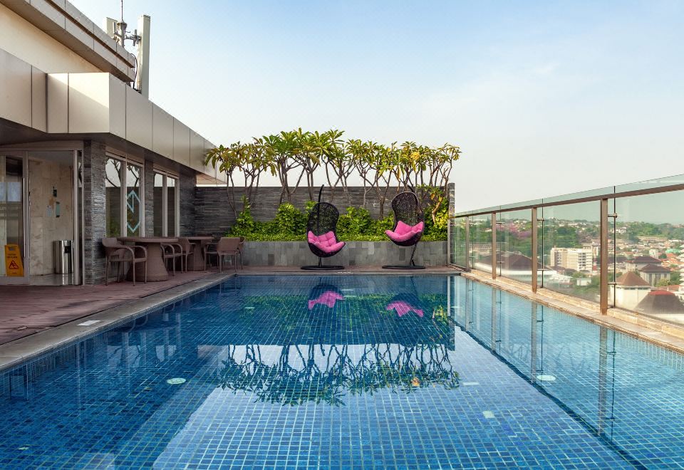a large swimming pool with two pink hammocks hanging from trees and a building in the background at Louis Kienne Hotel Simpang Lima