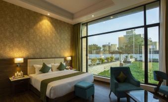 a large bed with white linens is in a room with a chair and window at Sarovar Portico, Somnath