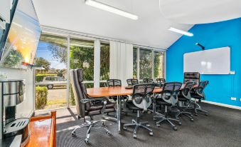 a conference room with a large wooden table surrounded by black chairs , and a window allowing natural light to enter the room at APX Parramatta