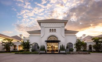 a large white building with a pointed roof and a glass door is surrounded by trees at Melia Vinpearl Cua Sot Beach Resort