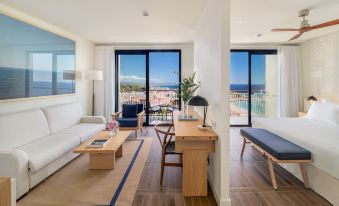 a living room with a couch , coffee table , and dining table is shown with a view of the ocean at H10 Imperial Tarraco