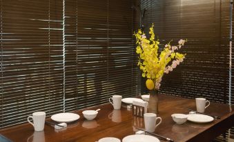 a dining table is set with white plates , bowls , and a vase of yellow flowers at M Hotel