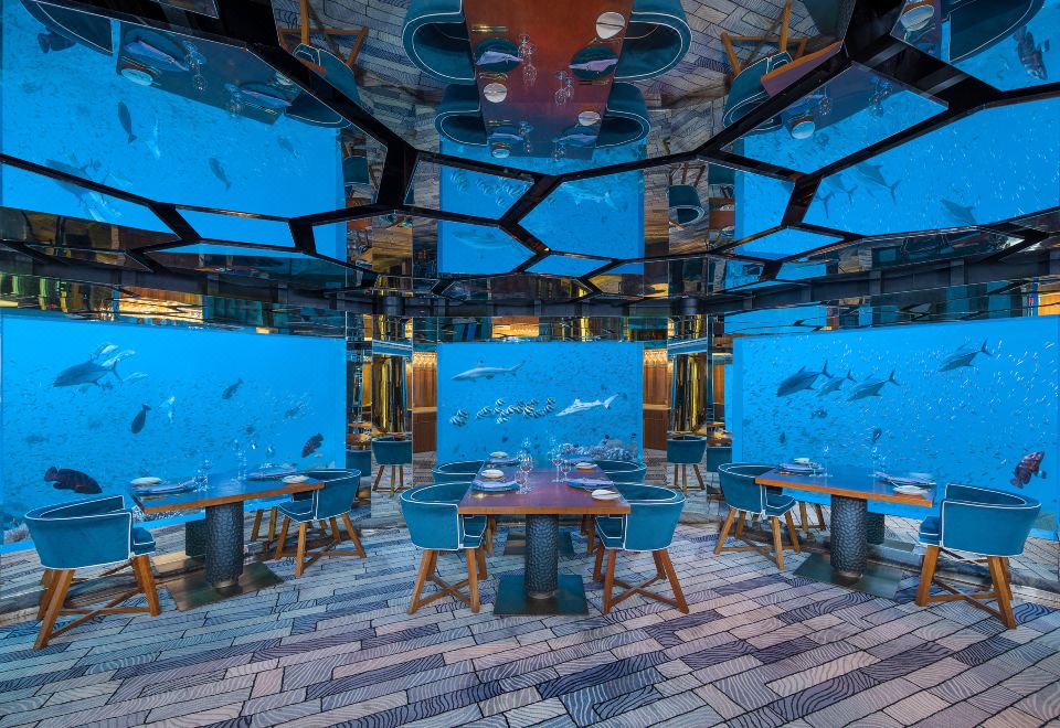 a large room with a blue ceiling and walls , filled with fish tanks and other underwater scenes at Anantara Kihavah Maldives Villas