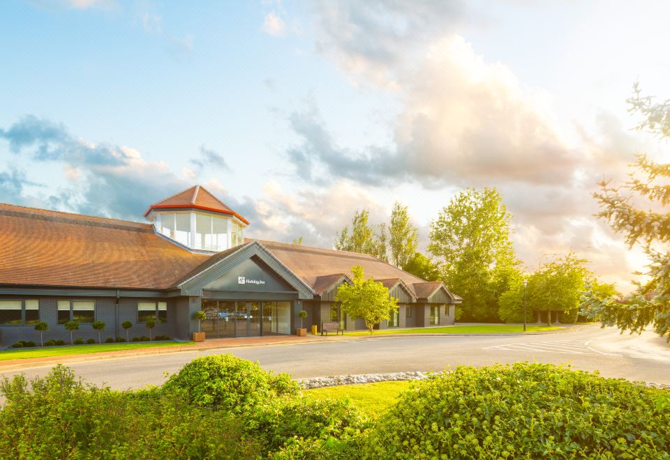 a large building with a red roof and a parking lot in front of it at Holiday Inn Aylesbury