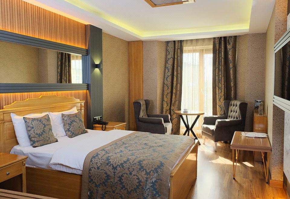 a hotel room with a king - sized bed , two chairs , and a tv . also a dining table in the room at Emirtimes Hotel&Spa - Tuzla