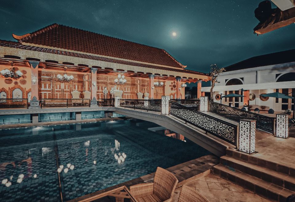 a nighttime view of a building with a large pool and wooden benches , surrounded by the moon at Ramada Suites by Wyndham Solo