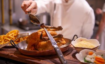a man is holding a ladle over a cooked chicken , preparing to serve it to someone at L'Hotel de Beaune