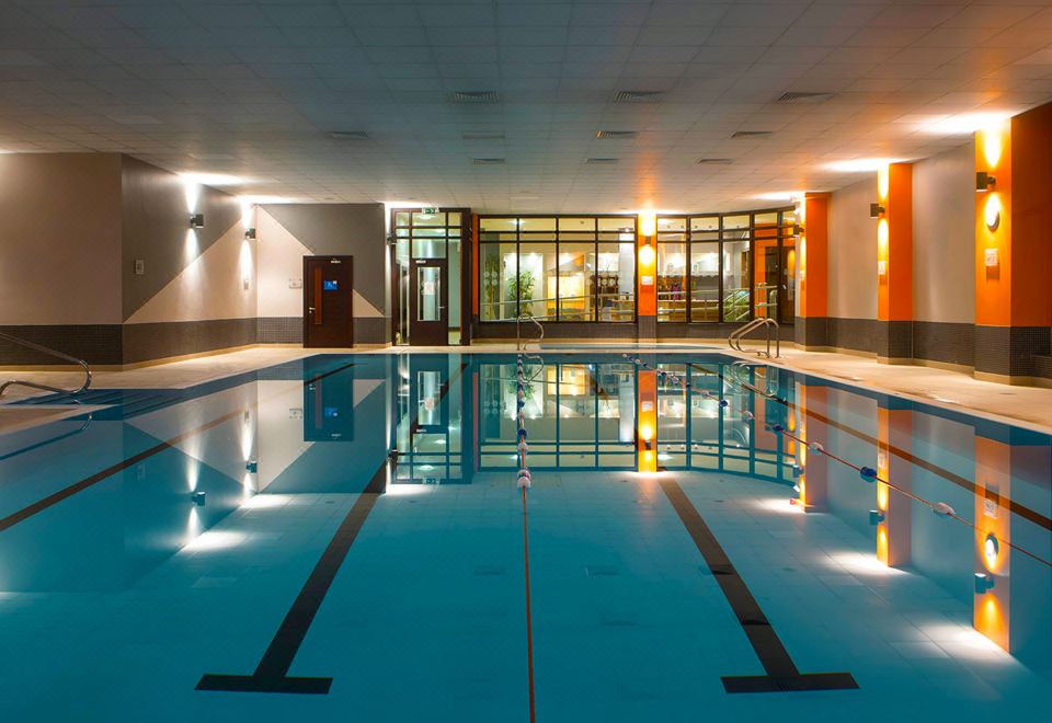 an empty indoor swimming pool with clear blue water and white tiles , surrounded by a modern building at Claregalway Hotel