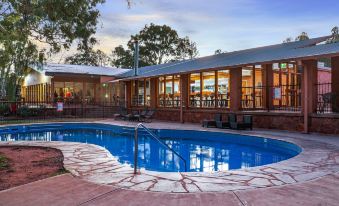 a large swimming pool is surrounded by a stone patio and has a building in the background at Discovery Resorts - Wilpena Pound