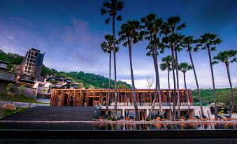 a modern building with wooden panels and palm trees , surrounded by a large pool and mountains at The Naka Phuket, a member of Design Hotels