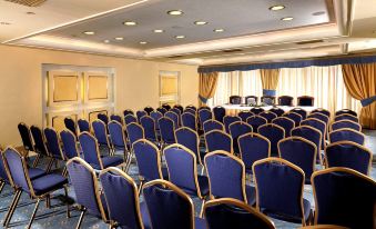 a large conference room with rows of blue chairs and yellow curtains , ready for an event at Savoy Hotel