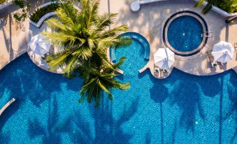 aerial view of a blue swimming pool surrounded by palm trees , with lounge chairs and umbrellas placed around it at Outrigger Khao Lak Beach Resort