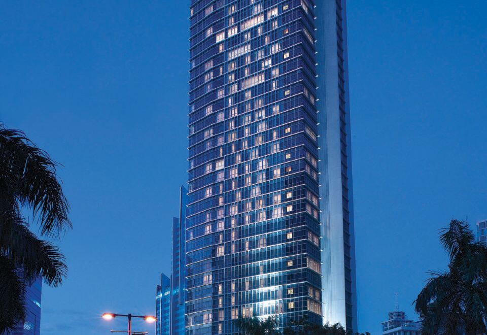 a tall building with a unique architectural design is lit up at night , surrounded by palm trees at Oakwood Premier Cozmo Jakarta