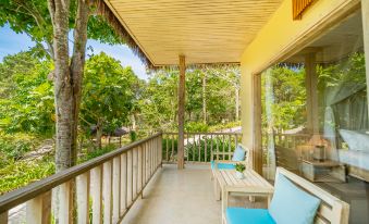 a wooden balcony overlooking a lush green garden , with a blue couch and chairs placed on the balcony at Lahana Resort Phu Quoc & Spa