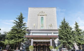 a large white building with a sign on the front , surrounded by trees and parked cars at Tibet Hotel