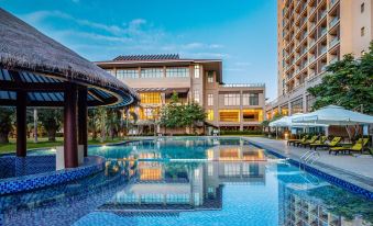 a modern hotel with a large swimming pool and umbrellas in front of it , surrounded by lush greenery at Sanya Xizang Hotel
