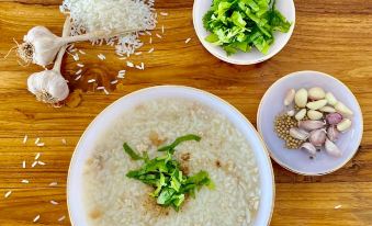 a wooden dining table with a bowl of rice and various side dishes , including garlic , lettuce , and onions at Funwan Hotel