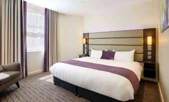 a large bed with a purple and white comforter is in a hotel room next to a window at Premier Inn Dover East