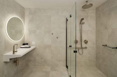 a modern bathroom with a glass shower enclosure , gray tiles , and a white countertop at Oval Hotel at Adelaide Oval, an EVT hotel