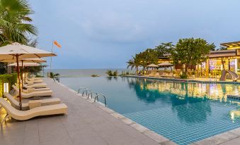a large swimming pool with lounge chairs and umbrellas is surrounded by palm trees and overlooks the ocean at Sand Dunes Chaolao Beach Resort