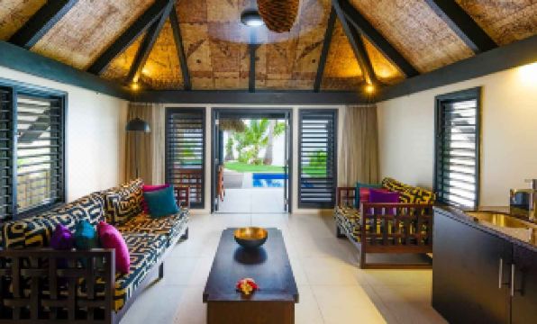 a living room with a couch , coffee table , and sliding glass doors leading to an outdoor pool at Matamanoa Island Resort