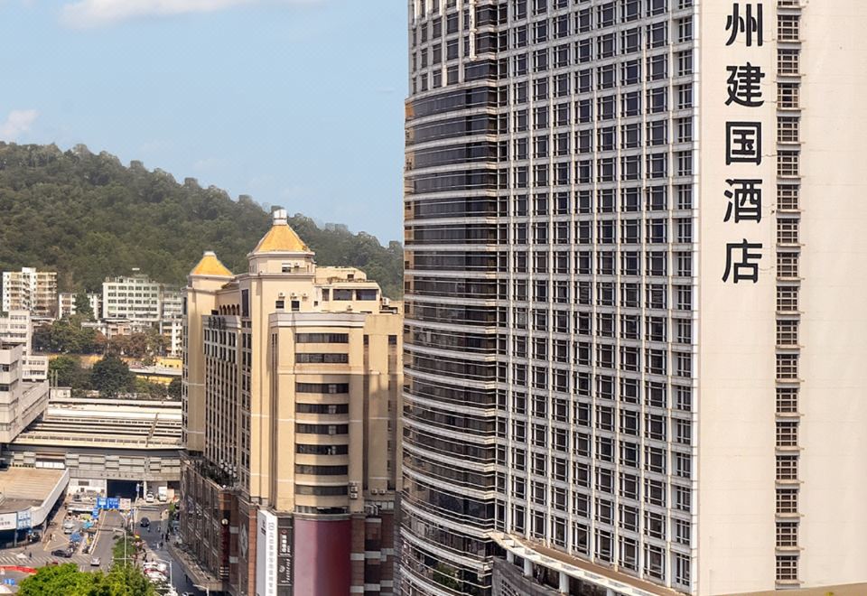 There is a large building with numerous windows surrounded by tall buildings, including an office tower at Jianguo Hotel, Guangzhou