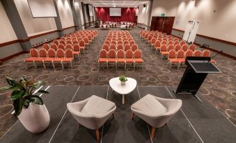 a large conference room with rows of red chairs and a podium at the front at Novotel Perth Langley