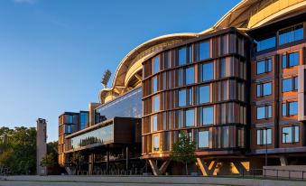 a modern building with a large glass facade and wooden accents , situated next to a park at Oval Hotel at Adelaide Oval, an EVT hotel
