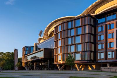 a modern building with a large glass facade and wooden accents , situated next to a park at Oval Hotel at Adelaide Oval, an EVT hotel