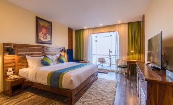 a large bed with white and blue bedding is in a room with wooden floors , a desk , and a window at Aagantuk Resort