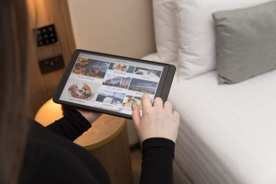 a woman is standing in a hotel room , holding a tablet computer with images on it at Oval Hotel at Adelaide Oval, an EVT hotel