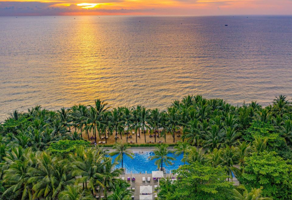 a luxurious resort with a pool surrounded by palm trees , as the sun sets over the ocean at Salinda Resort Phu Quoc - Sparkling Wine Breakfast