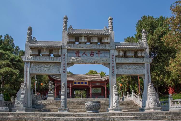 Wolonggang is on the west side of Nanyang City in Henan. It is where Zhuge Liang lived in seclusion and farmed, and the site of the famed "Three Visits to the Thatched Cottage" and the strategic discussions at the thatched cottage. The Wuhou Shrine on the ridge was first built during the Wei and Jin dynasties and flourished in the Tang and Song. It is a national 4A-level scenic area and a nationally protected key cultural relic site, and among Wuhou shrines nationwide, it is one of the earliest founded.

📍 Location: Wolonggang, Wolong District, Nanyang, Henan Province (Wuhou Temple In Wolonggang, Nanyang)
🕘 Opening hours: May 1–Sep 30, 8:00 AM–6:00 PM (last entry 5:30 PM); Oct 1–Apr 30 of the following year, 8:00 AM–5:30 PM (last entry 5:00 PM).
📌 The entire area closes at 6:00 PM. Wuhou Temple In Wolonggang, Nanyang Museum closes at 5:30 PM. Please keep the closing times in mind when planning your route.

⛩ "dragon among people through the ages" stone paifang arch
✨ Highlights:
· The stone paifang arch before the shrine stands 9 m tall and 13.5 m wide. With three gateways and four pillars in a tower-like form, it is richly carved and makes the first striking sight before you enter.
· The architrave bears the incised phrase "dragon among people through the ages," implying that Zhuge Liang was a dragon among mortals and hinting that Wolonggang is a land of hidden talent.
· First built in the Ming dynasty of bluestone, it rises layer upon layer when viewed from the steps below, with bracket sets and intricate patterns stacking upward.

🏛 Great worship hall and stele corridor
✨ Highlights:
· The great worship hall houses colored statues of Zhuge Liang, his son Zhuge Zhan, and his grandson Zhuge Shang. It is the main hall for offerings to Zhuge Liang through the ages.
· Along one side before the hall, the Ming dynasty stele corridor is inlaid with stone inscriptions of the first and second "Memorial on Sending Out the Troops" in Yue Fei’s calligraphy, whose vigorous strokes make it the shrine’s most eye-catching inscription.
· From the mountain gate to the great worship hall, the left and right corridors form the front sacrificial area. Ancient cypresses stand thick, and plaques and couplets line the way to the hall.

🛖 Cottage of Zhuge Liang
✨ Highlights:
· Also known as Zhuge Hermitage, the present thatched cottage is a brick-and-wood octagonal structure with projecting eaves and an outer octagonal corridor, its roof covered in thatch.
· A plaque inscribed "Cottage of Zhuge Liang" by Guo Moruo hangs over the main entrance.
· Behind the shrine, areas reflecting Zhuge Liang’s rustic life include Yeyun Hermitage, Ancient Cypress Pavilion, Companion Moon Terrace, and Tilling Pavilion, collectively known as the Ten Scenes of Wolong.

🌳 Ningyuan Tower and ancient cypresses in the shrine
✨ Highlights:
· Ningyuan Tower, also called Qingfeng Tower, stands at the rear of the shrine and serves as the concluding piece of the complex.
· The grounds contain over 200 old and notable trees. Ancient cypresses alternate with slender bamboo, making it noticeably cooler inside in summer.
· More than 150 historic buildings survive, and the number of plaques, couplets, and steles ranks among the most in Wuhou shrines nationwide.

💡 Travel tips: Many structures and steles are historic—please do not touch them. Turn off your camera flash. Stone steps connect the courtyards; they can be slippery after rain, so slow down. There are many ancient trees, and mosquitoes can be active in summer—bring insect repellent. The museum closes early, so we recommend entering earlier in the afternoon and allowing 2 hours.

🚗 Transportation
By car: navigate to "Wuhou Temple In Wolonggang, Nanyang." The scenic area sits on Wolonggang on the west side of Nanyang’s urban area, with parking lot(s) nearby.
Public transportation: take a high-speed train to Nanyang East Station, then transfer by bus or taxi. Multiple city bus routes reach Wolonggang.

Come to Wolonggang in Nanyang and walk the grounds of the Three Visits to the Thatched Cottage!