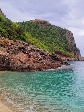 Турция.Алания.Must visit.

Место без которого невозможно представить путешествие в Аланию - гора с крепостью и башней KızılKule.  
Для полноценного осмотра необходим целый день, желательно не самый жаркий. 
Рекомендую начать с пляжа Клеопатры, который находится слева, если смотреть на гору с моря (первое фото). Далее спуститься в пещеру Дамлаташ (второе фото), посмотреть на сталактиты и сталагмиты, подышать целебным воздухом. Её посещение выписывают как лечение для пациентов с проблемами дыхательных путей. 
После этого пройти до фуникулера и подняться на гору, там открываются нереальные виды на обе стороны Алании, можно сделать много красивых фото и видео, чтобы передохнуть остановитесь на кофе или чай, который приготовит турецкая бабушка, в маленьком домашнем кафе на вершине. Можно взять аудиогид и послушать историю данного места на русском языке. 
Пришло время спускаться...если сделать это пешком, по асфальтированной дороге, по пути увидете несколько смотровых площадок с чарующими пейзажами.
Внизу зайдите в Красную башню и в гроты - бывшие верфи.
У крепостной стены есть семейное кафе - Mandarin, где можно отведать традиционные лепёшки со шпинатом, сыром, картошкой,  мясом, которые называются Гёзлеме. 
8 лет назад,когда я была здесь последний раз,  их делала бабушка, чья фотография висит на стене, сейчас  уже дело в руках  детей и внуков.
Если захочется искупаться, то можно спуститься к пляжу Терсане (минуты три пешком от кафе), только имейте ввиду, что переодевалок, лежаков и туалетов там нет, это узкая полоса песка вдоль крепостной стены, благодаря расположению здесь не бывает волн.
Если останутся силы, то прогуляйтесь по   порту, любуясь самыми разными кораблями и яхтами... 
Вот такой насыщенный день может у вас получиться, без группы, без  организованной экскурсии, в своём темпе, наслаждаясь каждым моментом❤️
#алания 