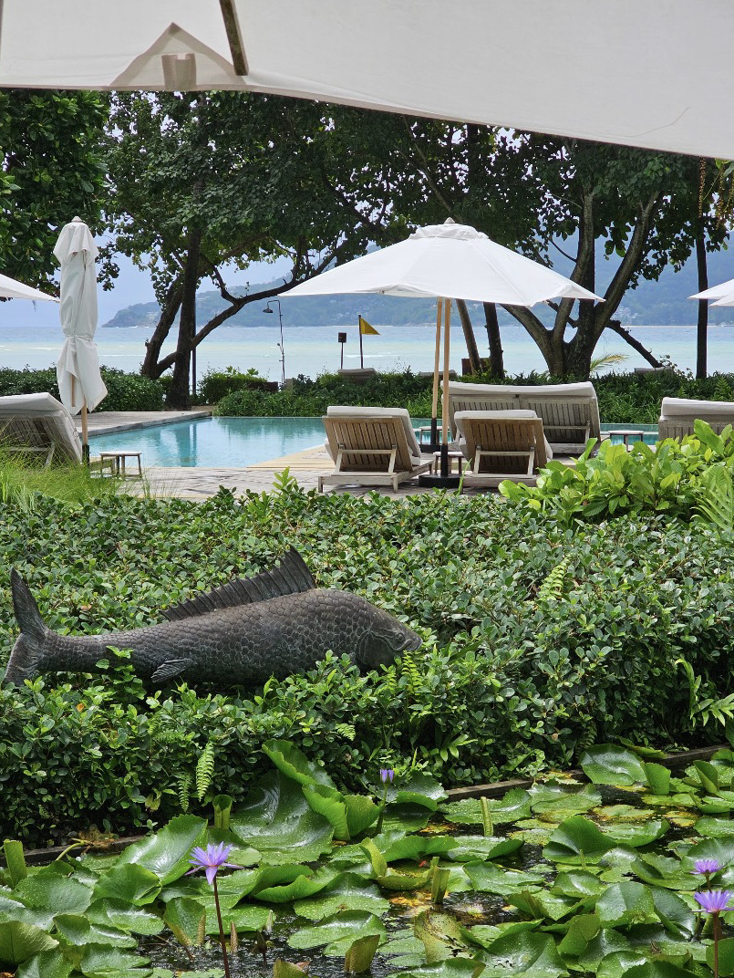 Rosewood Phuket is a luxury resort located on the serene Tri Trang Beach, offering a tranquil and private atmosphere. It is perfect for a relaxing getaway, just a short distance from the bustling Patong area. The resort is designed to blend harmoniously with nature, surrounded by lush trees and stunning views of the Andaman Sea, creating a relaxing ambiance in every corner.

The accommodations here come in the form of pavilions and private villas, decorated in a modern tropical style. Using wooden materials and natural tones, the rooms exude warmth. Many rooms feature private pools and spacious relaxation areas, making them ideal for couples or family vacations.

Another highlight is the premium-quality dining options, especially the Italian restaurant and beach club with an excellent atmosphere. Guests can enjoy meals while admiring the sea view and breathtaking sunsets. Additionally, the resort offers a spa, fitness center, and a variety of water activities.

With its luxury, natural surroundings, and attentive service, Rosewood Phuket is one of the best resorts in Phuket. It is perfect for a special getaway that combines tranquility, privacy, and a world-class experience.