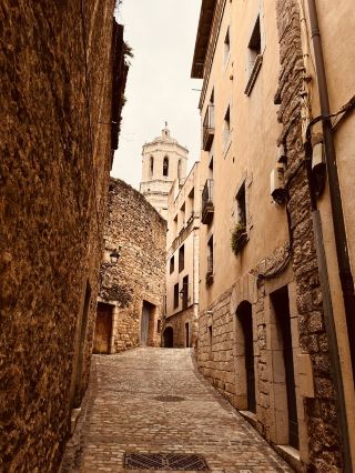 
西班牙赫羅納 (Girona) 位於加泰羅尼亞自治區,是一座融合了中世紀魅力與現代氣息的歷史名城,距離巴塞隆納僅約 1 小時車程。 
赫羅納大教堂 (Girona Cathedral): 以擁有世界第二寬的哥特式中殿聞名,其宏偉的 90 級台階是電視劇《權力的遊戲》(Game of Thrones) 中「貝勒大聖堂」的取景地。
彩色房子與埃菲爾鐵橋 (Pont de les Peixateries Velles): 奧尼亞河 (Onyar River) 畔色彩繽紛的房屋是城市名片。橫跨河流的紅鐵橋由巴黎埃菲爾鐵塔的設計師 Gustave Eiffel 設計。
猶太區 (El Call): 歐洲保存最完好的中世紀猶太社區之一,迷宮般的小巷極具氛圍。
中世紀古城牆 (Passeig de la Muralla): 沿著古老的城牆漫步,可以俯瞰整個老城區的壯觀全景。12月末的下午三、四點鐘,夕陽餘暉灑在古城中,感覺置身在童話世界裏。 