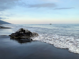 Nanganesa Beach, a black sand beach with white waves.