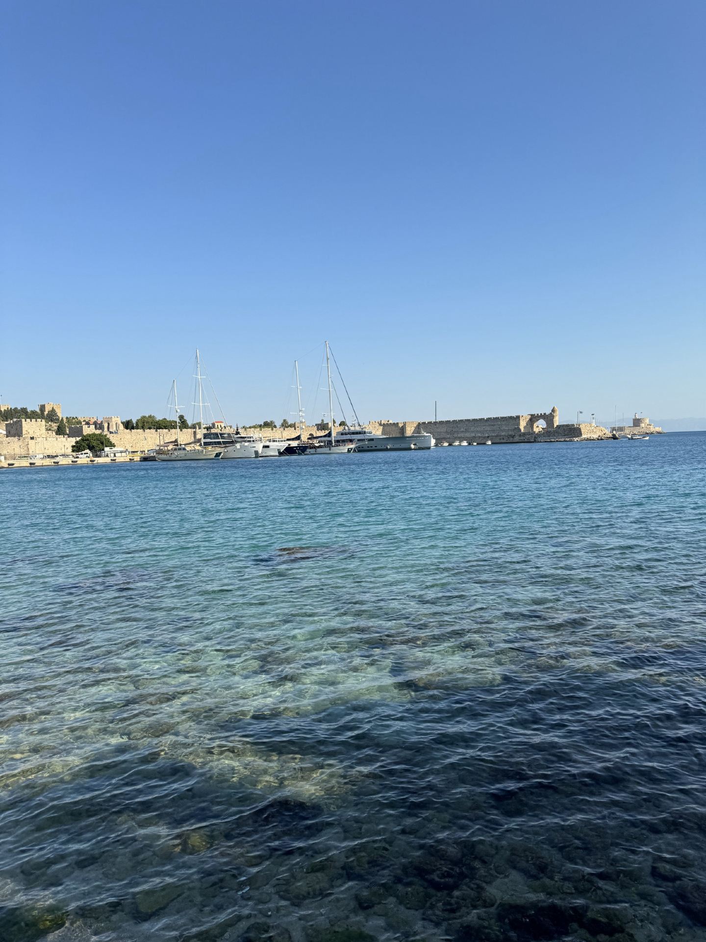 Ancient medieval walls on the left, the sun-kissed Aegean Sea on the right. Strolling along the Rhodes coastline.