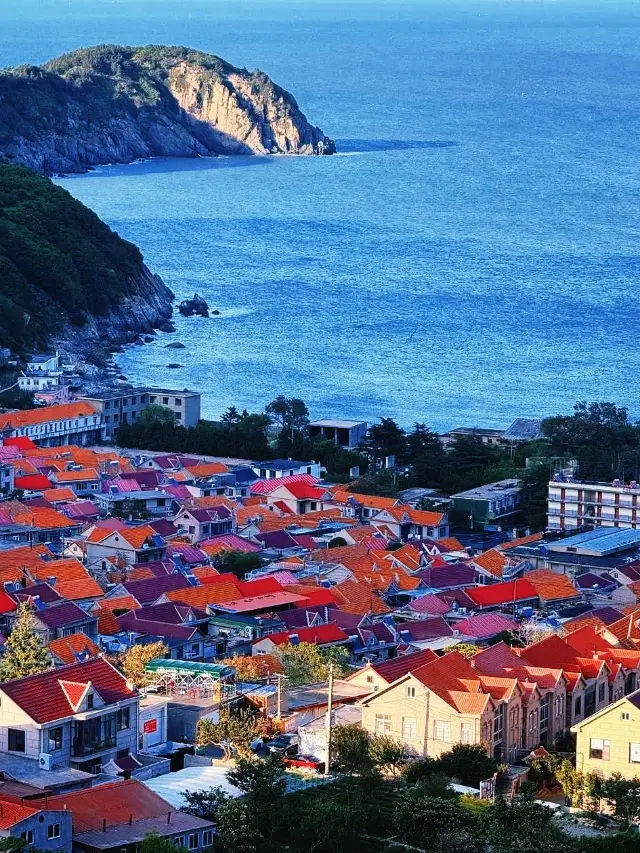 The red tiles, green trees, blue sea, and sky—the sunset at Qingshan Fishing Village in Qingdao is absolutely stunning