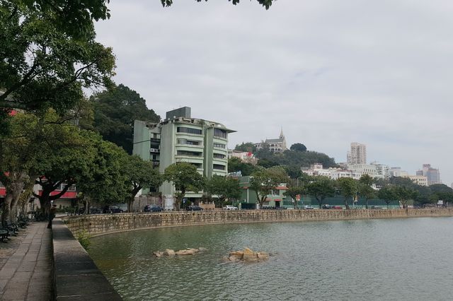The curved moon over the railing, the tranquil blue lake, the flowing water, the small bridge, and the secluded path.