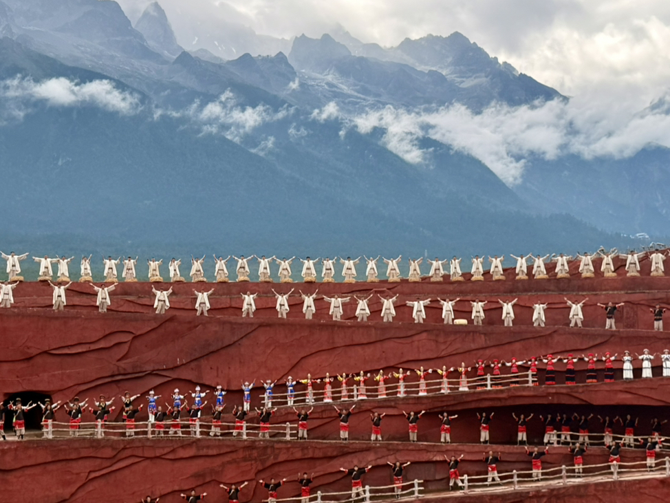 Impressions Lijiang: A Spectacular Show Against Snowy Peaks 🌄🎭  
Get ready to experience Impressions Lijiang—a jaw-dropping open-air performance at the foot of Yulong Snow Mountain. The natural mountain backdrop makes every scene feel epic, and the dazzling choreography will leave you absolutely mesmerized. It’s not just a show—it’s an immersion into Yunnan’s culture and landscape!

📸 Top Photo Spots:  
The best “insta-worthy” moment is during daylight, when the performers are framed perfectly against the snowy Jade Dragon Mountain. Capture panoramic shots from your seat, or head to the edge for those wide-angle landscape shots. The striking contrast of vibrant costumes with the serene mountain is a must!

🕒 Practical Tips:  
Shows typically run in the daytime, so bring sunglasses and a hat—sunlight can be intense! Dress in layers; mountain weather changes fast. Tickets sell out, especially in peak season, so book ahead. And be prepared—the performance is outdoors, so rain can happen (a raincoat is way better than an umbrella!).

⚠️ Precautions:  
Altitude can be tiring—pace yourself and drink plenty of water. If you’re sensitive to sun, don’t forget sunscreen!

#Lijiang #YulongSnowMountain #OutdoorPerformance #CulturalTravel #TravelTips