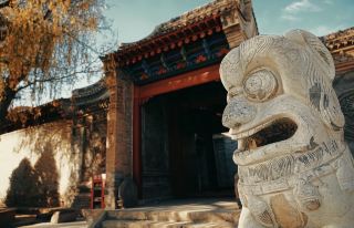 The red walls and gray tiles frame the weathered stone lions, and the "Fu" character on the lanterns carries the warmth of the autumn breeze