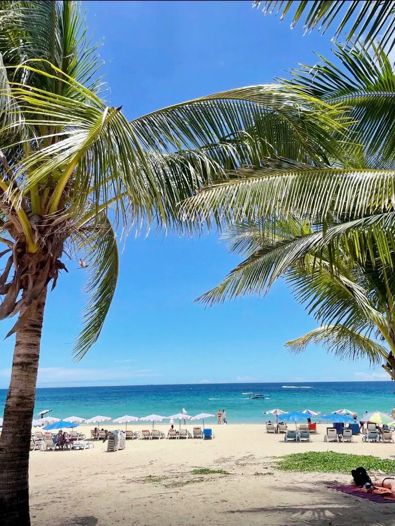 What greets you here is not a bustling crowd, but a long stretch of golden sand and gentle waves. Walking along the beach, the soft and comfortable fine sand cushions your feet, while a breeze carrying the scent of sea salt lightly brushes your face. Sunlight dances on the sea's surface, creating shimmering silver-white sparkles, enveloping the entire world in a soft glow.

In the distance, the horizon merges with the sky, and the sea displays layers of blue hues. The interplay of light on the water and in the sky evokes a sense of calm and vastness. Swaying coconut trees along the shore add a tropical charm, compelling you to pause, sit on the beach, and watch the waves gently lap against the shore.

Unlike popular tourist spots, Karon Beach is not crowded, allowing visitors to truly enjoy leisure and freedom. There's no need for elaborate plans; simply strolling, sunbathing, or listening to the sound of the waves is enough to relax your body and mind. Every grain of sand and every drop of seawater here reminds travelers to slow down and fully embrace the tranquility of the sun, sea breeze, and the serene connection between the ocean and sky.