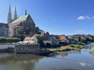 格爾利茨(Görlitz)位於德國薩克森州最東端,與波蘭城市茨戈熱萊茨(Zgorzelec)隔尼斯河(Neisse)相望,人口約5.7萬人,是德國保存最完好的歷史城市之一。格爾利茨擁有約4000座受保護的歷史建築,由於二戰末期城市幾乎未遭大規模破壞,因此完整保留了從中世紀、文藝復興、巴洛克到19世紀的建築風貌。聖彼得及保羅教堂(St. Peter und Paul)始建於15世紀,是城市最具代表性的哥特式建築地標。上下市場廣場周圍環繞著色彩豐富、裝飾精美的歷史建築,展現了中世紀商貿城市的繁榮景象。連接德國格爾利茨與波蘭茨戈熱萊茨的跨境步行橋象徵兩國友好關係,也是遊客喜愛的觀景地點。憑藉保存完整的城市景觀,格爾利茨成為歐洲著名的電影取景地之一,曾作為《布達佩斯大飯店》(The Grand Budapest Hotel)的主要拍攝地點,其中老百貨大樓更是影片中飯店內部場景的重要取景地。