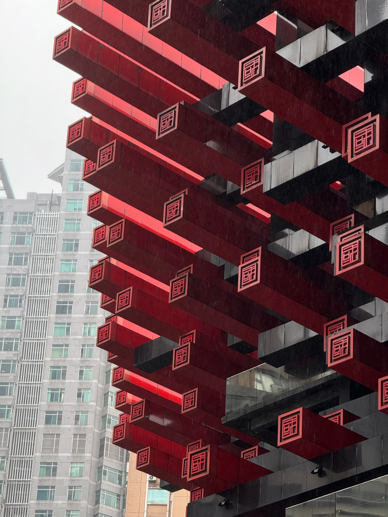 When I first spotted this building in Chongqing, my immediate thought was: what on earth is that?

At first glance, it looks like a colossal art installation or a sci-fi pagoda from the future. Red and black beams jut out in every direction, and the whole structure looks like it was pieced together defying laws I don't fully understand 😅

It turns out, this is the Chongqing Art Museum—the city's fine arts museum.

The architecture here is inspired by traditional Chinese wooden structures, but reimagined with a modern, almost cyberpunk twist. Honestly, even if you skip going inside (like I did), the place is totally worth checking out just for the building itself.

It looks especially striking in the rain—the wet pavement, the fog rolling between the skyscrapers, and this bizarre structure create a vibe like you're caught somewhere between ancient China and a futuristic sci-fi movie.

📍 Location:
Jiefangbei District, downtown Chongqing

🚇 Nearest Subway:
Linjiangmen Station

📸 Pro Tip:
Try visiting on an overcast day or in the evening—the atmosphere gets even more cinematic.