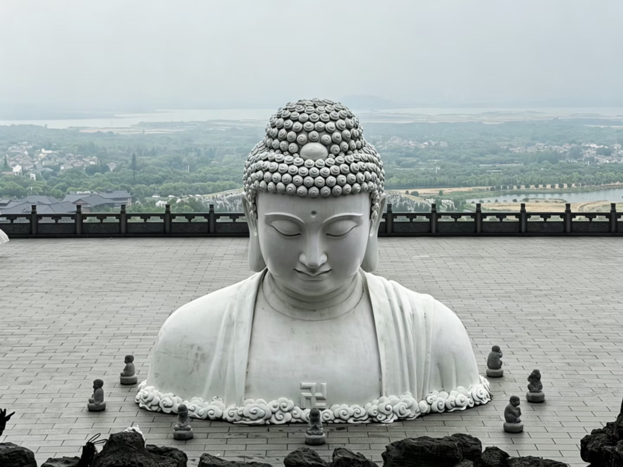 If you're visiting Nanjing and looking for a breathtaking hidden gem where your photos will look like scenes straight out of a classic Chinese period drama, I highly recommend pinning "Donglushan Guanyin Temple" in the Lishui District!
This ancient temple has a long history and is a branch of the Jiming Temple. The temple complex is built into the steep slopes of Mount Donglu, surrounded by lush green mountains with Zhongshan Lake stretching out in front. The atmosphere is incredibly peaceful. If you visit on a slightly misty day, the gentle breeze carrying the sound of wind chimes will absolutely melt your heart.

📸 Must-See Highlights (as seen in the photos):
1. The Maitreya Buddha and Dragon Stone Stairs: Walk up the stone stairs beautifully flanked by golden deity statues.
2. The Giant White Buddha Bust: The most magnificent highlight sitting in the middle of a spacious stone courtyard. From behind it, you get an endless panoramic view of the city and the lake. Any angle you shoot from looks serene and powerful.
3. Rock Garden and Fountain Pool: Features Zen-style stone sculptures, including the hand of Guanyin pouring water from a willow vase. This spot gives off incredibly relaxing vibes.
4. The Resident Cats: Adorable little kitties (sporting four white "socks") waiting to greet pilgrims along the way.

💡 [Travel Tips] How to get there easily, quickly, and on a budget!
Since the temple is located about 40-50 kilometers from downtown Nanjing, if you're not driving yourself, I recommend this exact route for the "ultimate time and money saver."
 🚇 Step 1 (Cheap & Fast): Take the Nanjing Metro Line S7 and get off at Lishui Station (溧水站). This helps you dodge city traffic, and the fare is super cheap.
 🚗 Step 2 (Most Convenient): Once you exit the metro station, just grab a taxi or use the DiDi app and pin "东庐山观音寺" (Donglushan Guanyin Temple). It's a 10+ kilometer ride and way faster than waiting for a local bus. If you split the fare with friends, it's just a few RMB per person.

📌 Additional Info for Travelers:
 Admission Fee: Free! (Free Entry) Parking is also free. It's a totally worthwhile spot.
 Opening Hours: 08:00 AM - 05:00 PM (Interior halls start closing at 04:30 PM, but you can still stroll around and take photos in the outdoor courtyards).
 Recommended Time to Visit: Go early in the morning before 10:00 AM or late in the afternoon between 03:00 PM - 04:30 PM. The lighting is gorgeous, and it’s not too crowded.
 Things to Note: The hike up involves quite a few stone steps, so it's highly recommended to wear sneakers or comfortable, slip-resistant walking shoes. It can also get pretty windy at the top, so if you're visiting on an overcast day, bringing an umbrella or a light jacket is a great idea.
If you're planning a trip to Nanjing, drop by to pray for blessings and soak in the breathtaking ancient Chinese architecture here. I guarantee you'll be impressed! 🙏✨