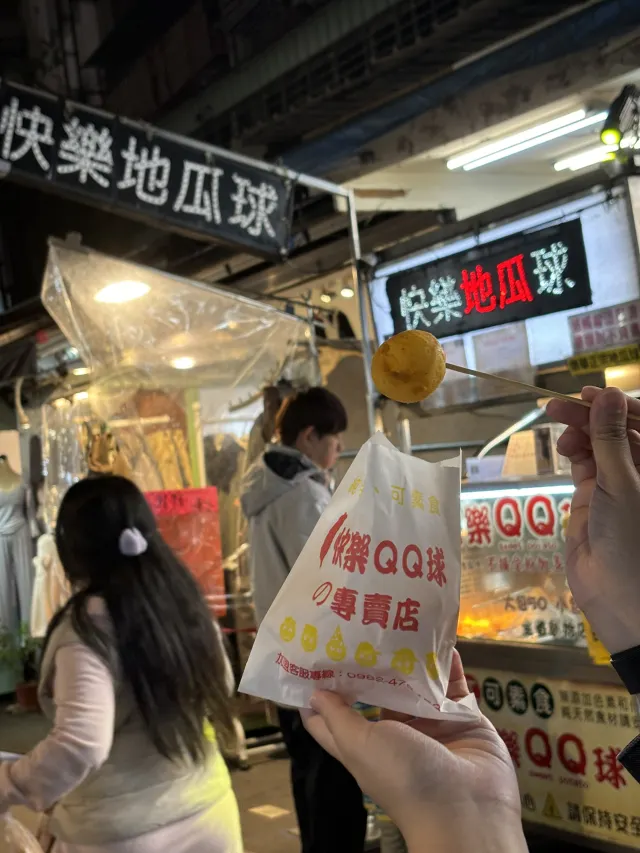樂華夜市的地瓜球攤，招牌寫著快樂地瓜球與樂QQ球，一串剛起鍋的地瓜球