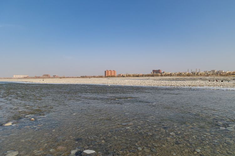 The Yurungqash River flows through Hotan in Xinjiang, rising on the north slope of the Kunlun Mountains. Because Hotan jade is found in the river, locals call it the White Jade River. In summer, snowmelt and calving glaciers in the Kunlun Mountains wash jade gravels into the river. Over millions of years, the current has polished them into white jade pebbles, and a few even become top-grade mutton-fat jade.
📍 Location: Hotan City, Hotan Prefecture, Xinjiang Uyghur Autonomous Region (river section along Yurungqash River Avenue)
🕘 Opening hours: Open 24 hours.
📌 Actual operating status depends on conditions that day. During the summer snowmelt, the water runs high. If you plan to go down to the riverbank to look for stones, choose a time when the water level is stable.

💧 The White Jade River and Hotan jade
✨ Highlights:
· In Old Uyghur, "Yurung" means "white." The river was named for its white jade (mutton-fat jade), and locals still call it the White Jade River.
· Each summer, as snow melts and glaciers fracture and collapse, floods carry jade gravels and ice into the river. After millennia of polishing by the current, the gravels become white jade pebbles.
· After joining the parallel Karakash River (the Black Jade River) to the west, the Yurungqash River forms the Hotan River, the largest river on the north slope of the Kunlun Mountains, which eventually flows into the Tarim River.

🪨 Riverbanks and jade picking
✨ Highlights:
· To enhance visitor experiences, the local government has designated a jade-picking experience zone on the east bank of the Yurungqash River, where visitors can legally enjoy looking for jade within marked areas.
· The riverbed is covered with water-rounded cobbles, with colors ranging from bluish-gray to milky white. Stepping on them produces a delicate crunching sound.
· You can still spot jade diggers on the riverbank. They turn over stones with pickaxes and shovels, and may work all day without finding a good piece.
· Looking south from the riverbank, the Kunlun snowline gleams in the distance, and the river changes color with the sky.

💎 Hotan jade markets
✨ Highlights:
· Walk along Yurungqash River Avenue in Hotan City and you will find several sizable Hotan jade markets on both sides, offering everything from rough stones to finished pieces.
· These markets used to be dominated by street stalls. Today, they are larger and more professional. If you want to quickly learn to judge the quality of Hotan jade, this is the best place to look around.

💡 Travel tips: During the summer snowmelt, the water level can rise very quickly. A seemingly gentle riverbank can turn into a rushing torrent at any time. Do not enter the water or dig for jade in the river, to avoid getting trapped. In the markets, compare carefully and buy only what you need. Be especially cautious with high-priced rough stones. Hotan has strong sun and frequent sand and wind. Bring a hat and sun protection.

Come to Hotan and walk the jade road along the White Jade River!
